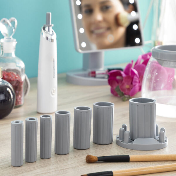 Kit Completo de Limpeza de Pincéis para Idosos Mulher idosa utilizando espelho iluminado enquanto demonstra as partes do kit de limpeza automática de pincéis de maquilhagem sobre uma base organizadora
