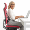 Idosa sorridente usando cadeira ergonómica com apoio lombar enquanto trabalha no computador