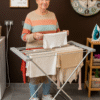 Idosa usando estendal elétrico dobrável InnovaGoods com 8 barras e 120W para secagem rápida e segura de roupa
