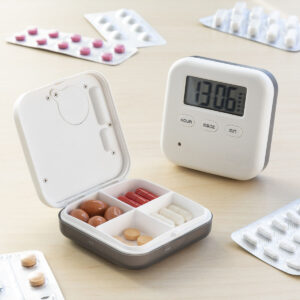 Idoso segurando alarme digital branco para medicação, com visor LCD e botões, ideal para lembrar horários de remédios