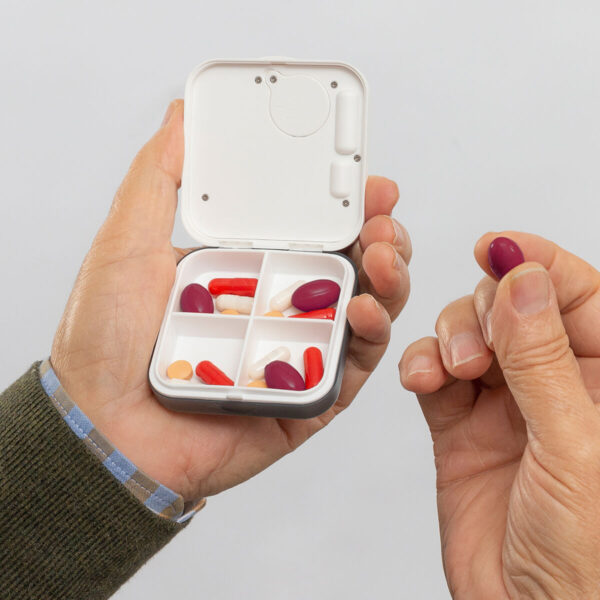 Caixa Portátil para Medicamentos com Compartimentos – Ideal para Idosos Mão segurando caixa portátil branca para medicamentos com compartimentos e pílulas