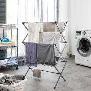 Cesto de roupa ao lado de estendal dobrável metálico em piso cerâmico