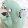 Mini máquina de costura portátil verde com botão de ajuste, ideal para idosos costurarem em casa com facilidade.