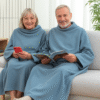 Casal entre 50 e 60 anos relaxando no sofá com cobertor duplo azul InnovaGoods, ideal para conforto, leitura e inverno.